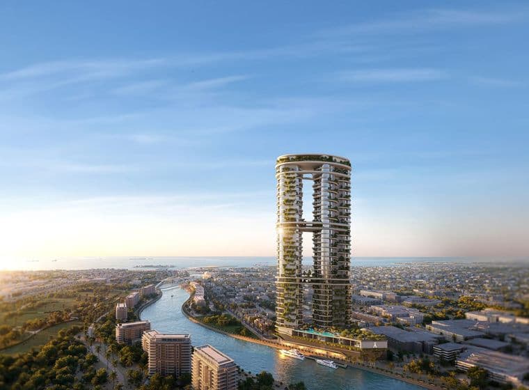 Two circular towers linked by a sky bridge, covered in greenery, rising beside a winding canal with boats and a distant city under a blue sky.