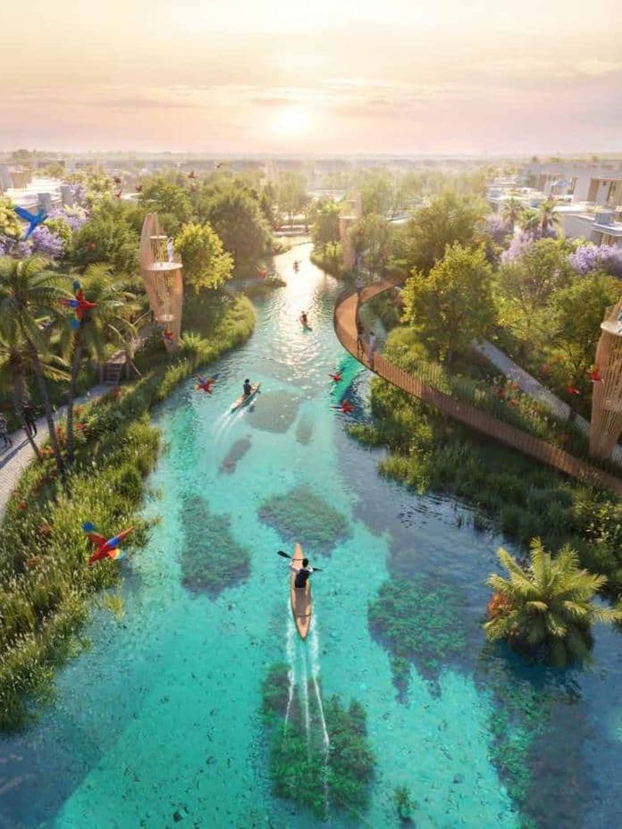 A serene canal winds through a lush modern residential area at sunset, with kayakers in the water and colorful birds in the trees.