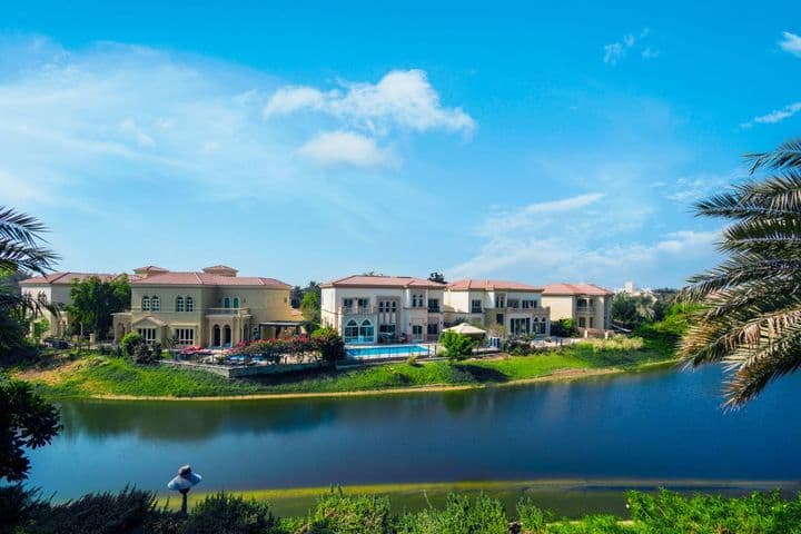 Luxurious lakeside villas with red-tiled roofs, surrounded by lush greenery under a clear blue sky, reflected in the tranquil water.