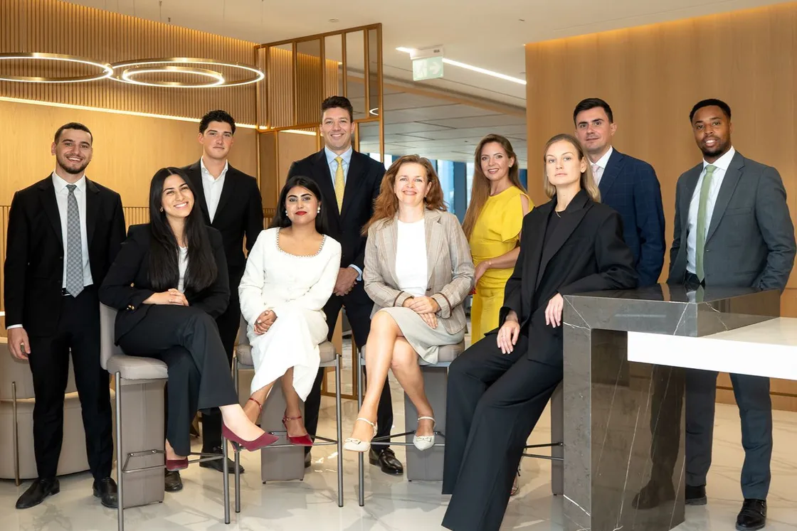 Diverse team of business professionals in formal attire posing and smiling in a modern office lounge.