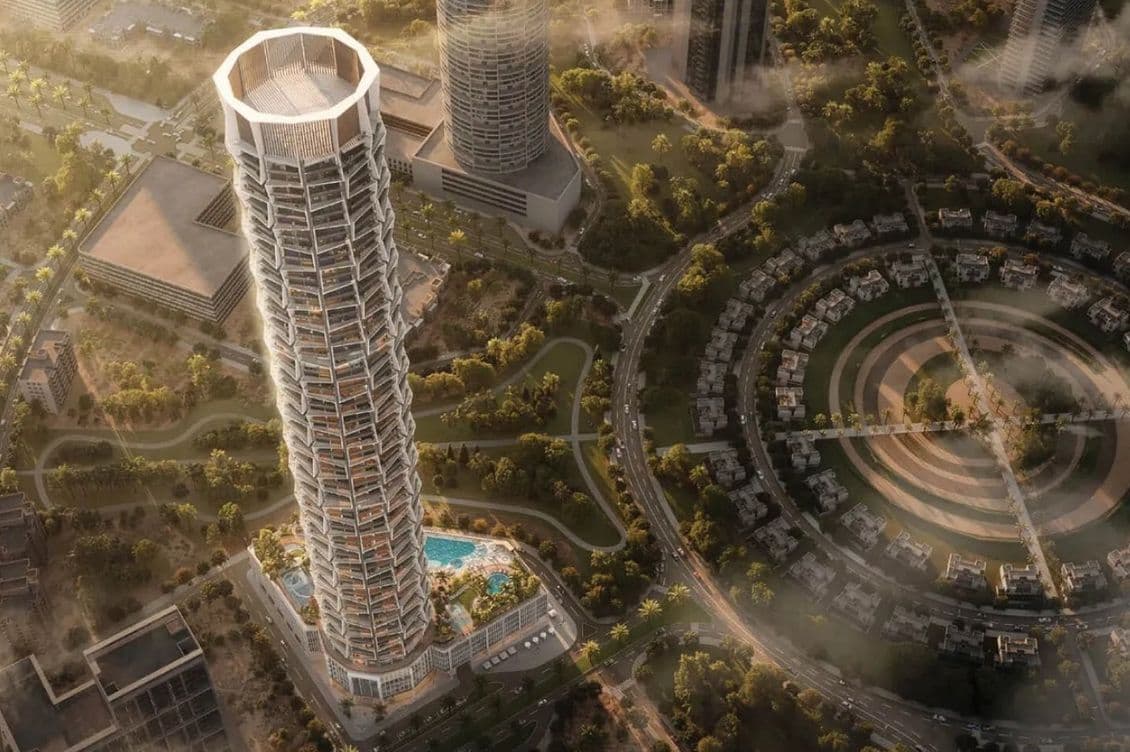 Aerial view of a tall, modern skyscraper, Binghatti Circle, with a unique geometric design, surrounded by greenery and circular structures in an urban setting.
