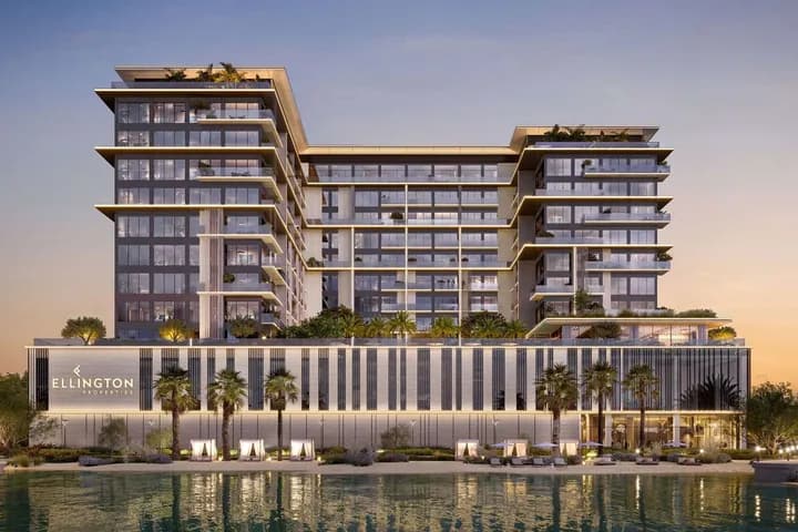 Luxurious glass-fronted, U-shaped waterfront building with stacked balconies, palm trees, and a lit podium reading Ellington Properties at sunset.