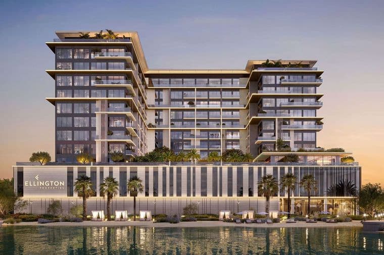 Luxurious glass-fronted, U-shaped waterfront building with stacked balconies, palm trees, and a lit podium reading Ellington Properties at sunset.
