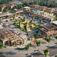 Aerial view of a modern shopping plaza with multiple buildings, outdoor seating, and landscaped areas surrounded by trees and roads.