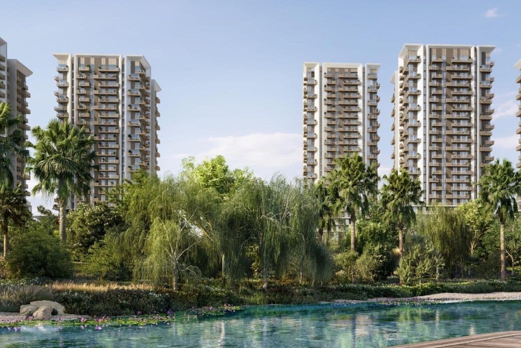 Tall modern apartment buildings at Rise By Aldar surrounded by lush greenery and palm trees, with a clear blue pond in the foreground under a sunny sky.th stre