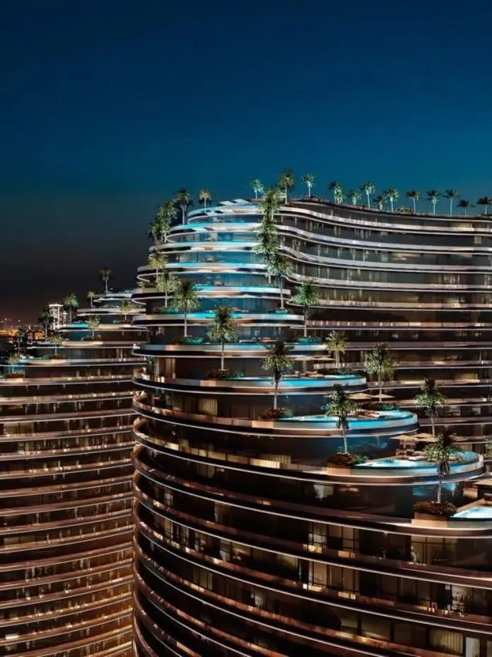 Night view of modern, multi-tiered buildings with rooftop pools and palm trees, set against a city skyline illuminated by lights.