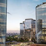Three modern glass office towers with reflective facades at dusk, mid-rise building with rooftop greenery and distant city skyline.