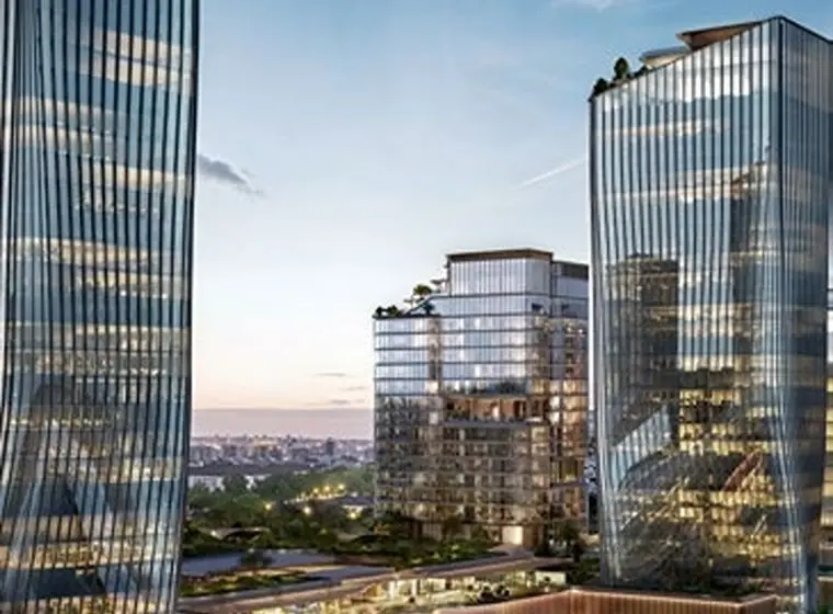 Three modern glass office towers with reflective facades at dusk, mid-rise building with rooftop greenery and distant city skyline.