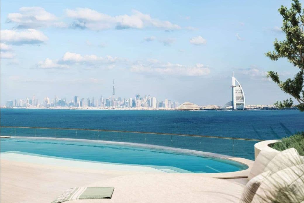 A luxurious poolside view overlooking the ocean, with Dubai's skyline and the Burj Al Arab in the background under a partly cloudy sky.