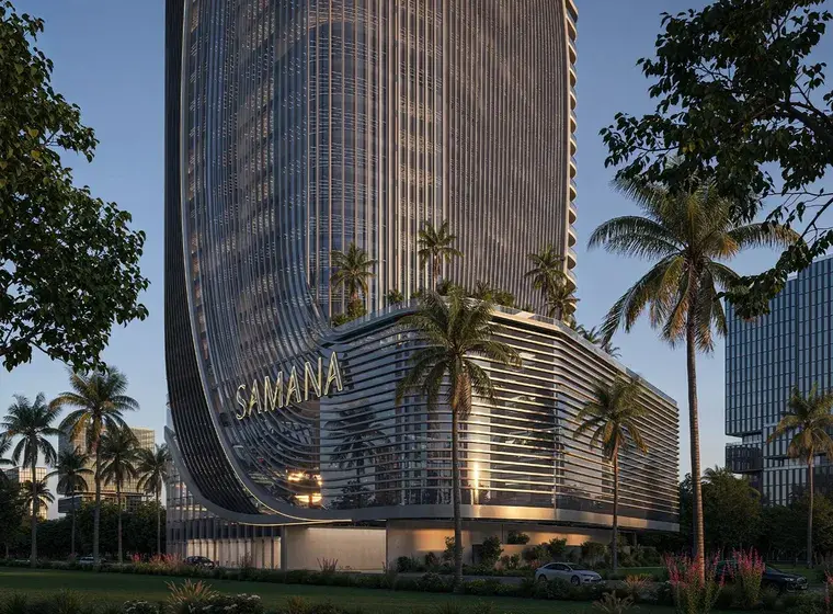 A futuristic glass high-rise with a curved, wave-like façade and a SAMANA sign on its base, surrounded by palm trees and tropical landscaping.