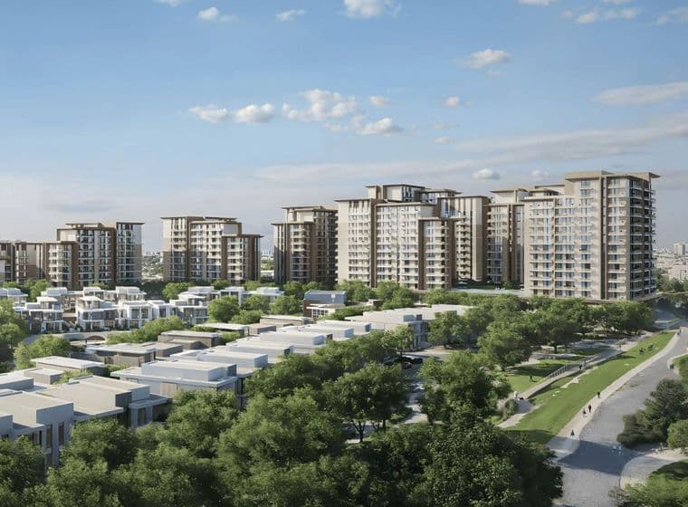 Modern apartment buildings surrounded by green trees and smaller residential structures under a blue sky with scattered clouds.