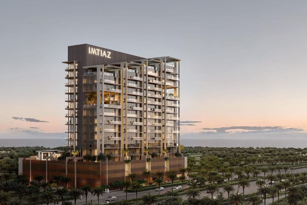 Tall, modern building with "IMTIAZ" sign at sunset, surrounded by palm trees, adjacent to a road, with a view of the horizon.