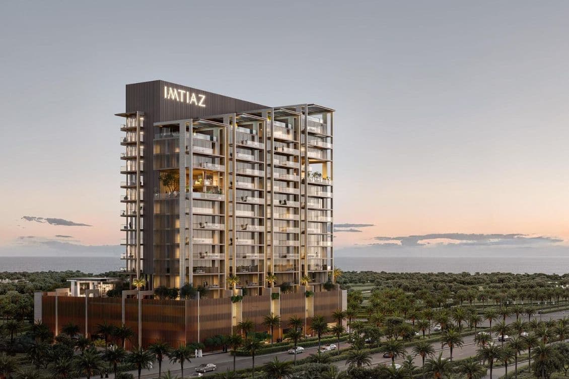 Tall, modern building with "IMTIAZ" sign at sunset, surrounded by palm trees, adjacent to a road, with a view of the horizon.