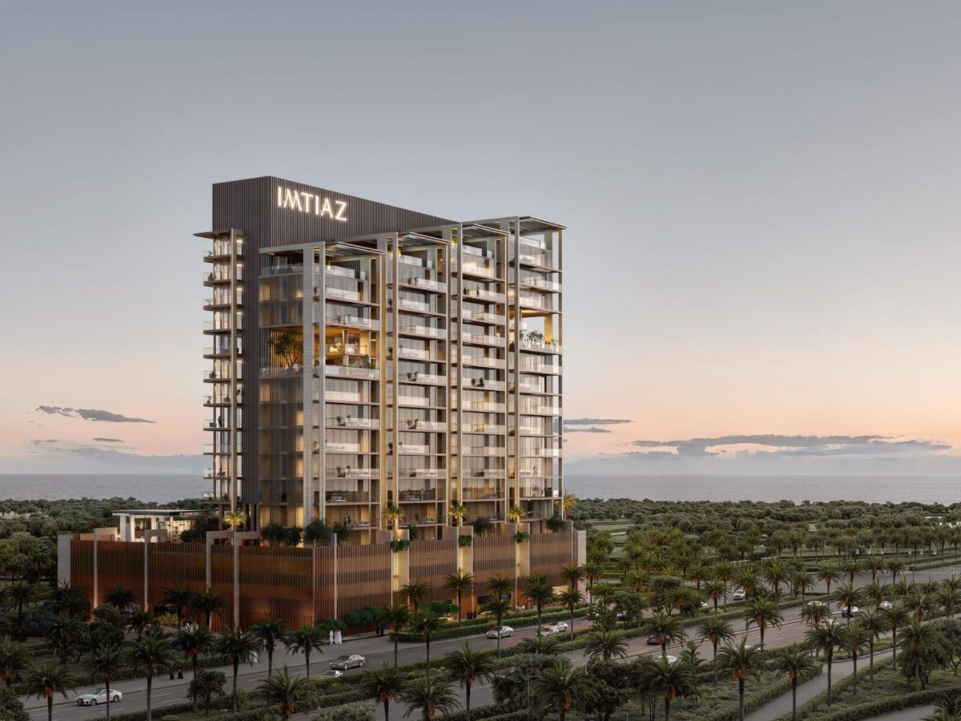 Tall, modern building with "IMTIAZ" sign at sunset, surrounded by palm trees, adjacent to a road, with a view of the horizon.