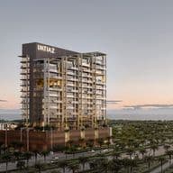 Tall, modern building with "IMTIAZ" sign at sunset, surrounded by palm trees, adjacent to a road, with a view of the horizon.