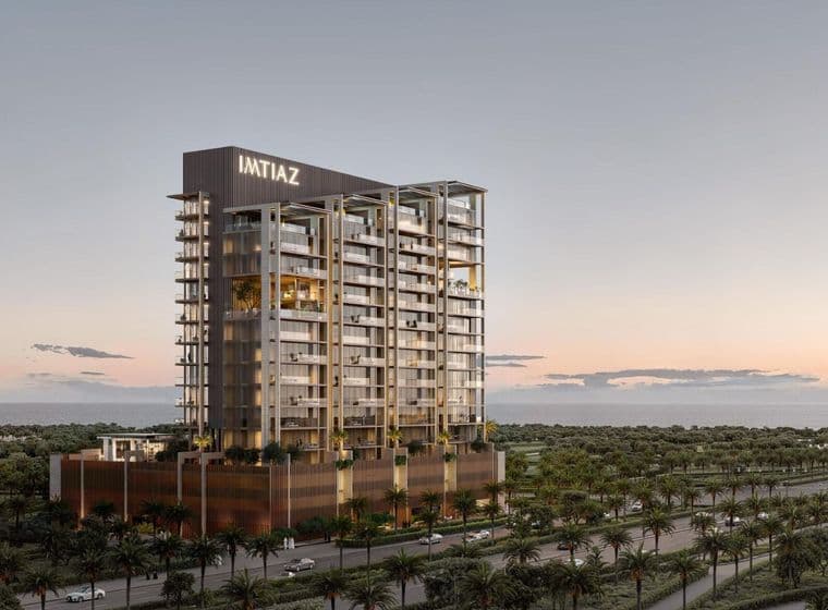 Tall, modern building with "IMTIAZ" sign at sunset, surrounded by palm trees, adjacent to a road, with a view of the horizon.