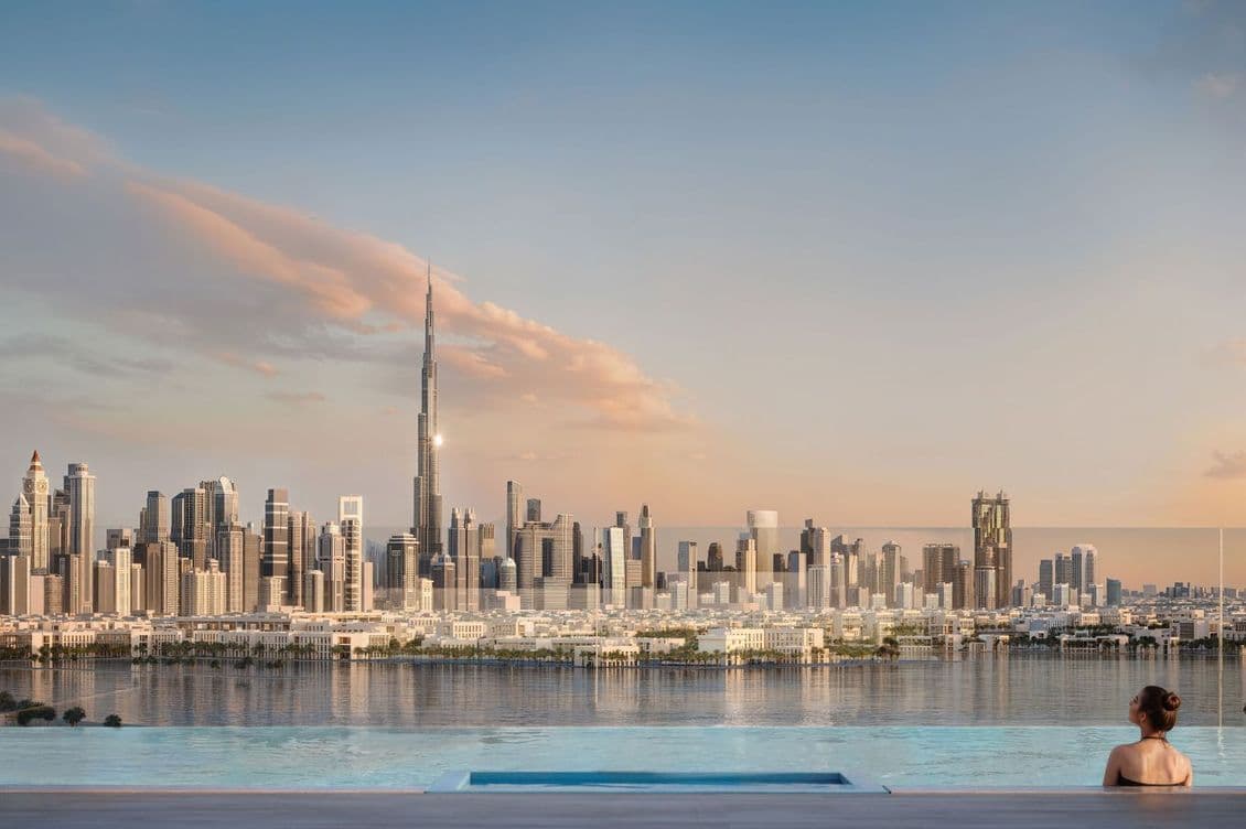 A person relaxes by a pool overlooking a city skyline with skyscrapers at sunset, featuring Burj Khalifa and a partly cloudy sky.