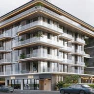 Modern multi-story building with glass balconies, lush plants, and sleek design. Ground level has shop entrances and parked cars in front.