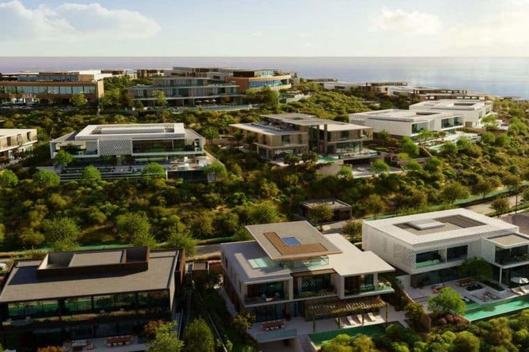 Luxurious modern villas on a lush hillside overlooking the ocean under a clear sky.
