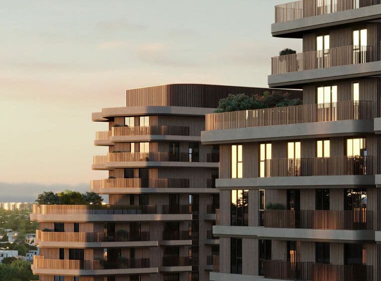 Modern multi-story buildings with sunlit balconies and rooftop greenery against a soft, evening sky.