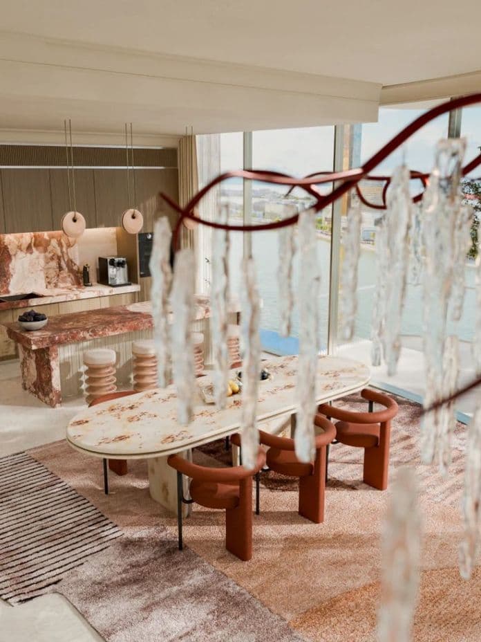 Modern dining area with a marble table, brown chairs, and large windows. Decorative light fixture and warm-toned decor create a luxurious ambiance.