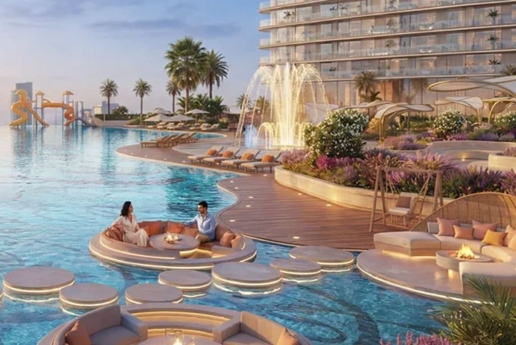 Luxurious resort pool area with decorative platforms, couples seated around mini fireplaces, a large fountain, lounge chairs, and palm trees.