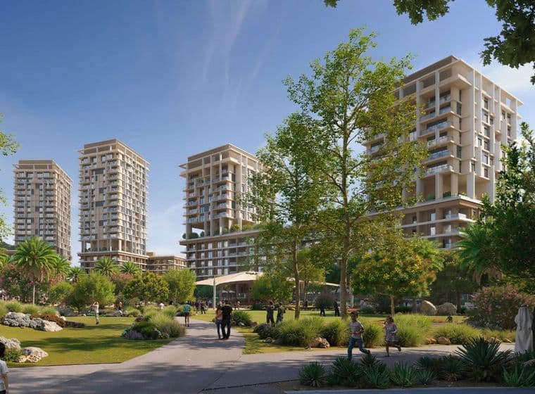 People strolling in a green park with pathways and trees, foregrounding modern high-rise apartment towers under a clear blue sky.