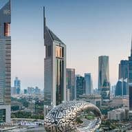 Dubai skyline with futuristic glass skyscrapers; foreground features a large white ring covered in Arabic calligraphy.