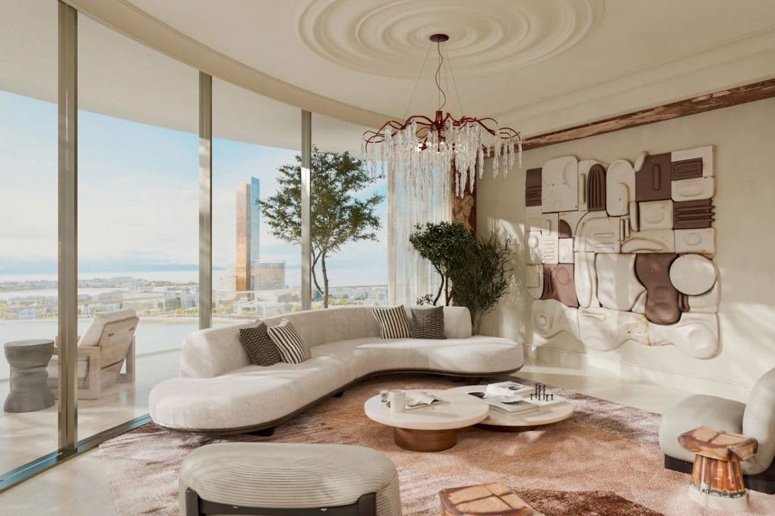 Modern living room with a curved white sofa, large windows offering city views, a chandelier, abstract artwork, and a round coffee table.