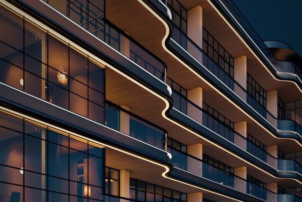 Modern building with curved balconies and glass windows, illuminated by warm lighting, viewed from a low angle at night.
