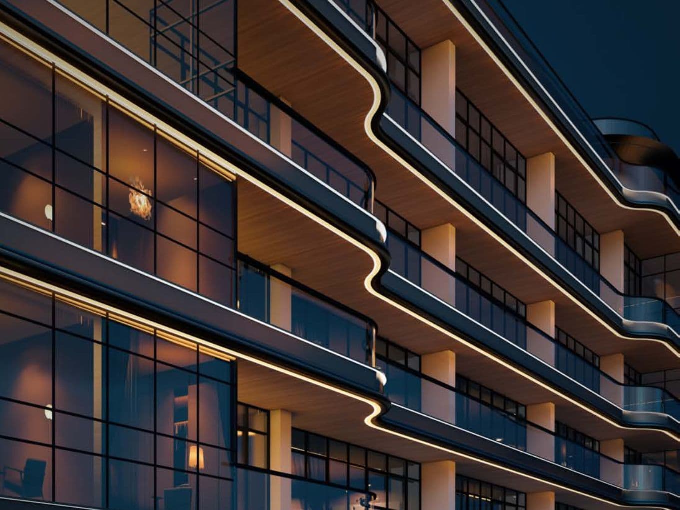 Modern building with curved balconies and glass windows, illuminated by warm lighting, viewed from a low angle at night.