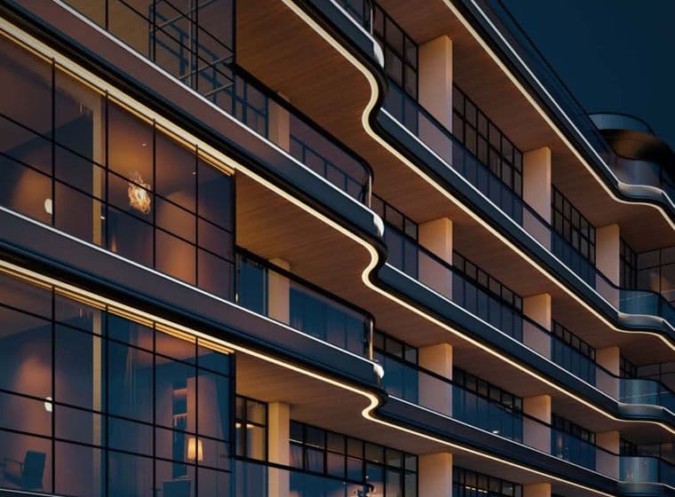 Modern building with curved balconies and glass windows, illuminated by warm lighting, viewed from a low angle at night.
