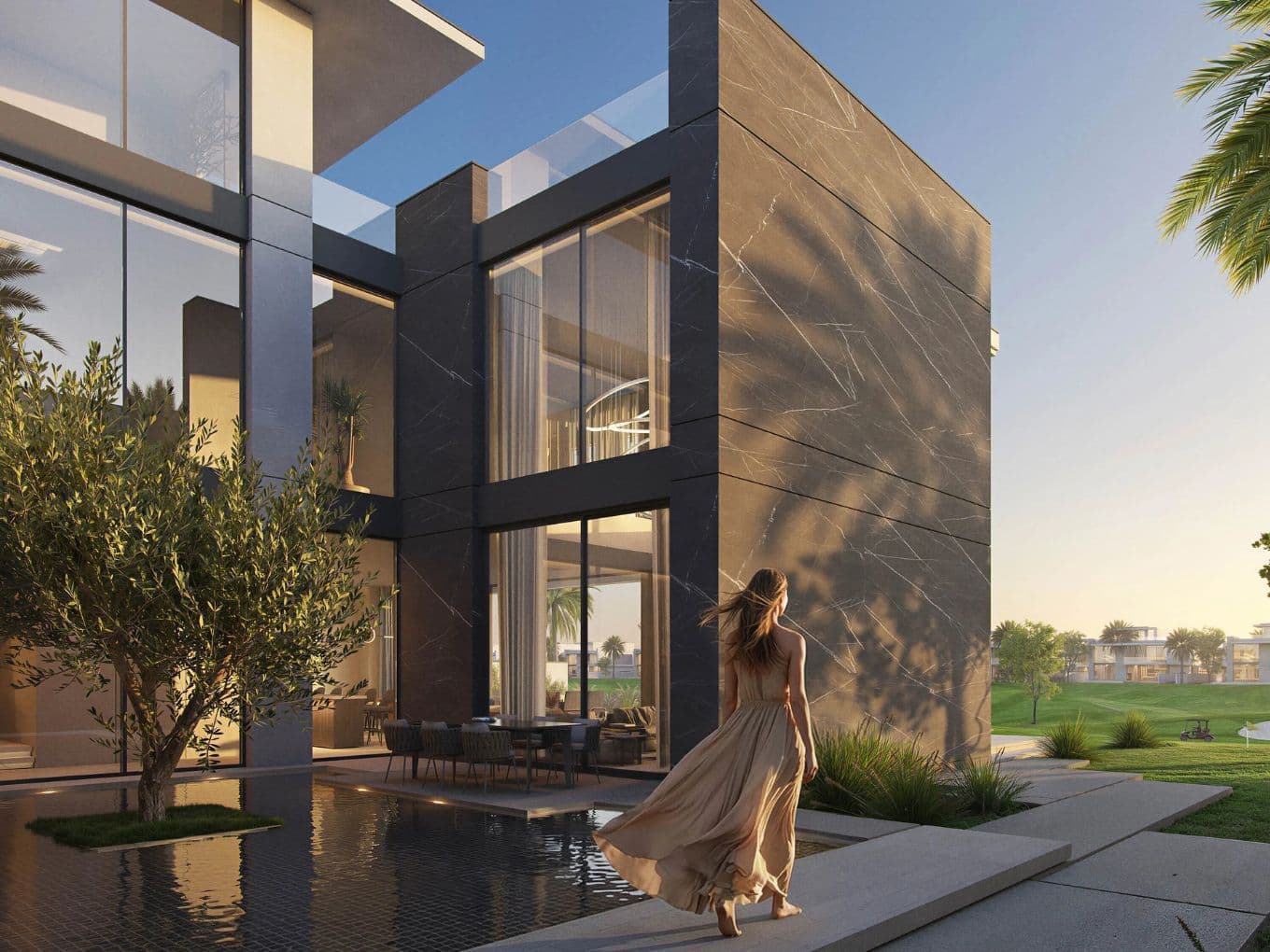 Woman in a flowing dress walks by a modern house with large windows, beside a reflective pool at sunset.