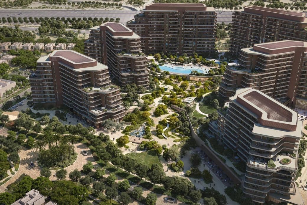 Aerial view of modern, curved apartment buildings surrounding a central garden with trees, paths, and a pool in an urban landscape.