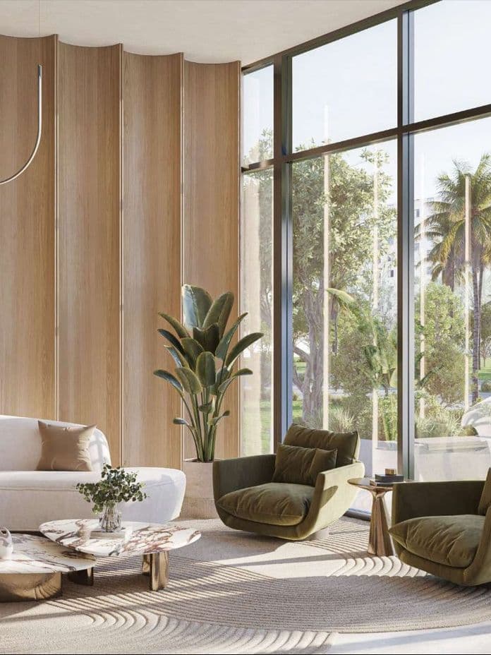 Modern living room with a white sofa, green armchairs, marble coffee tables, and large windows overlooking a garden with palm trees.