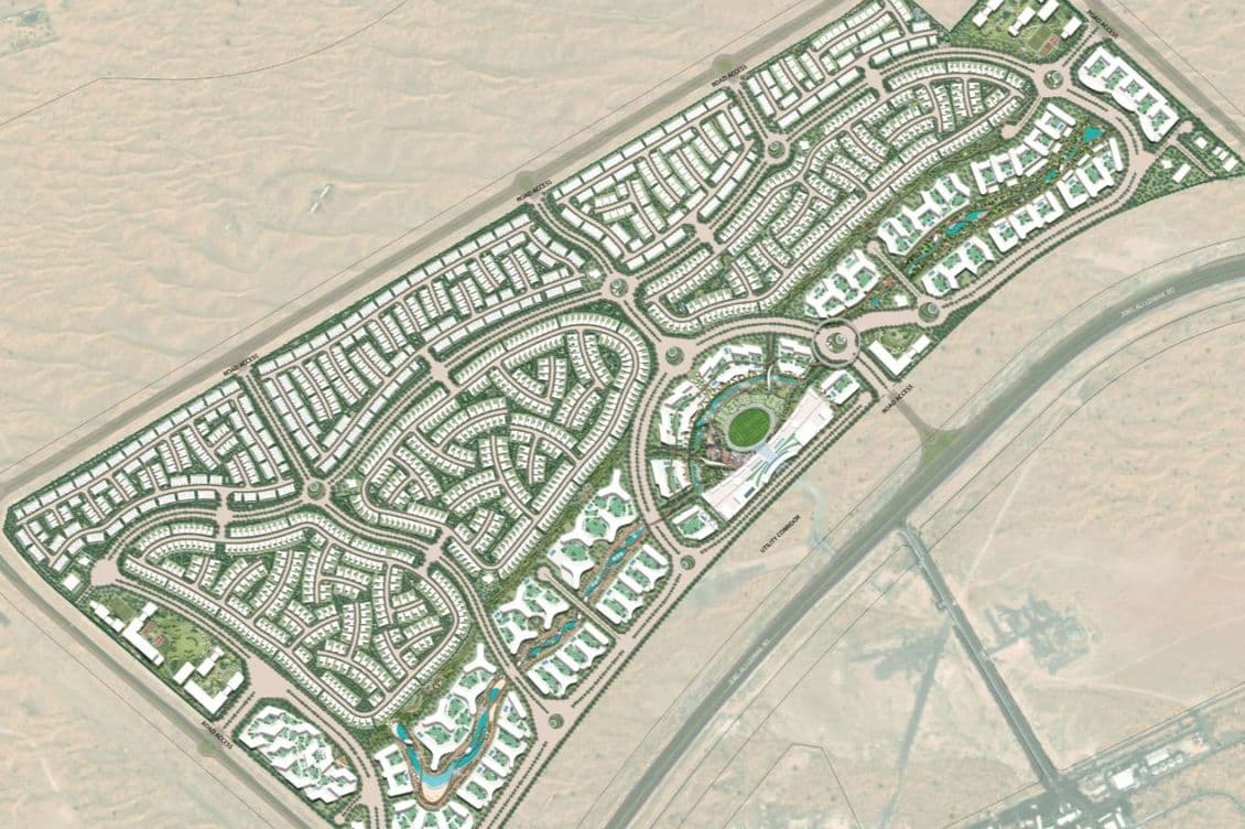 Aerial view of a planned community layout in the desert, featuring curved streets, green spaces, and buildings arranged in a grid pattern.