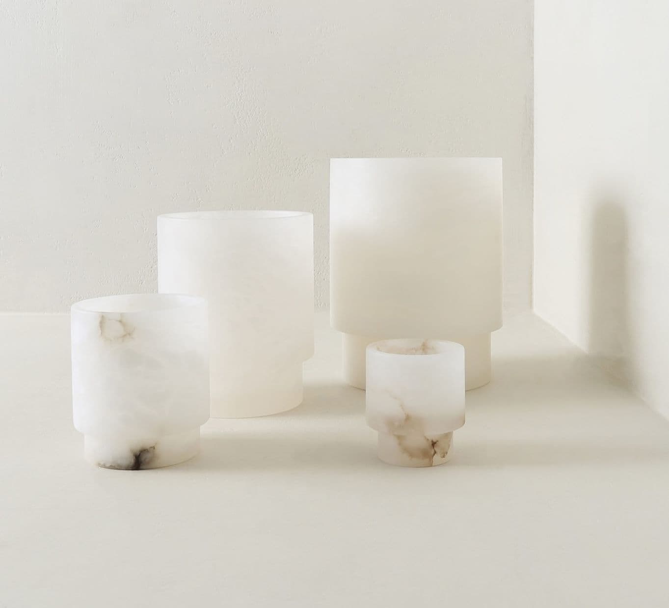 Four white marble-like cylindrical vases of varying sizes on a light textured surface.