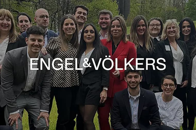 A group of Engel & Völkers real estate agents pose outdoors, smiling at the camera. The agents are wearing business attire in black, red, and gray.