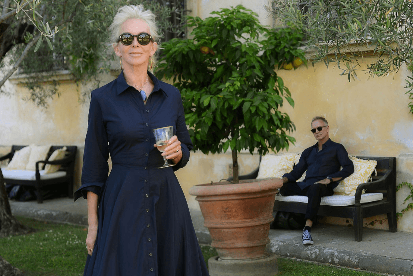 Trudie Styler standing in her garden in front of Sting sitting on a bench.