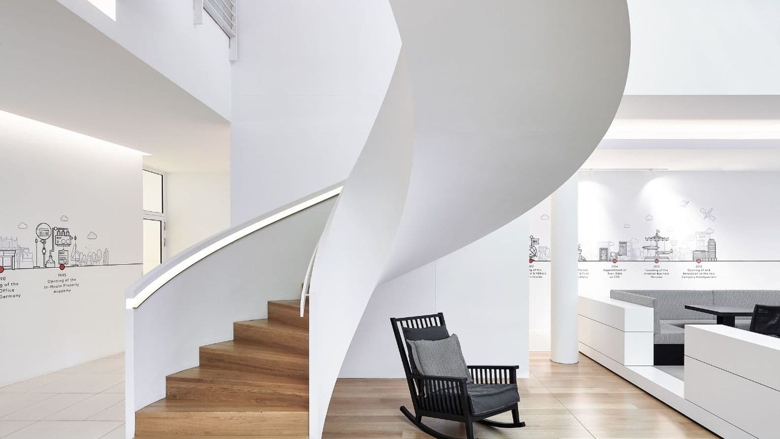 Modernes Interieur mit einer geschwungenen Treppe, Holzstufen, einem schwarzen Schaukelstuhl und Wandbildern, die eine Zeitleiste architektonischer Wahrzeichen zeigen.