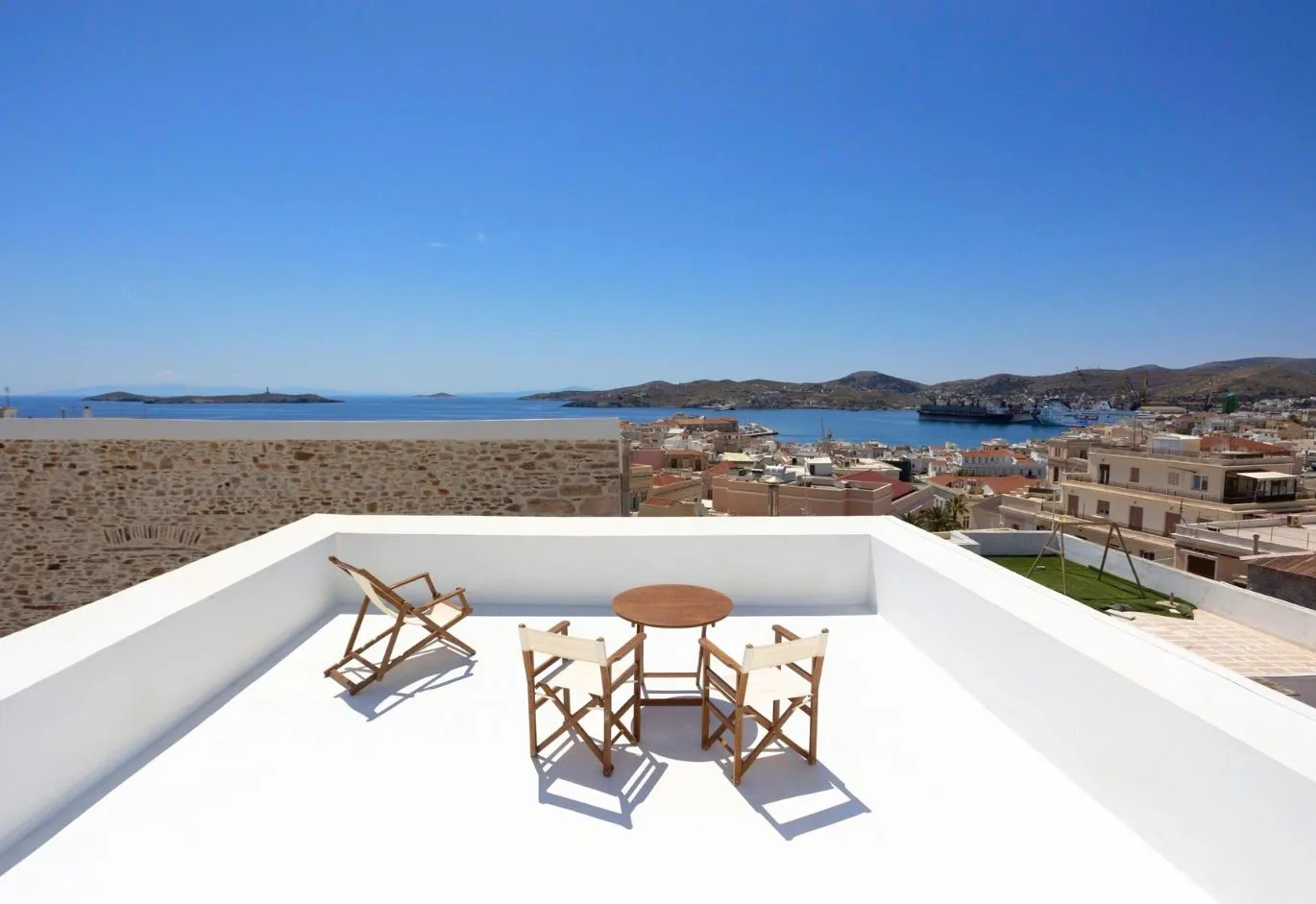 Rooftop terrace with wooden chairs and table overlooking a coastal town and the sea