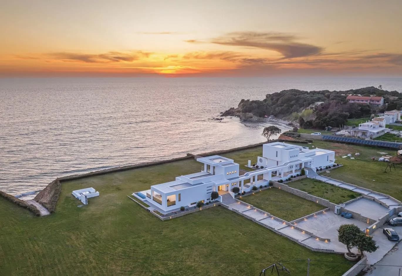Aerial view of a luxury modern white villa complex on the coastline during sunset
