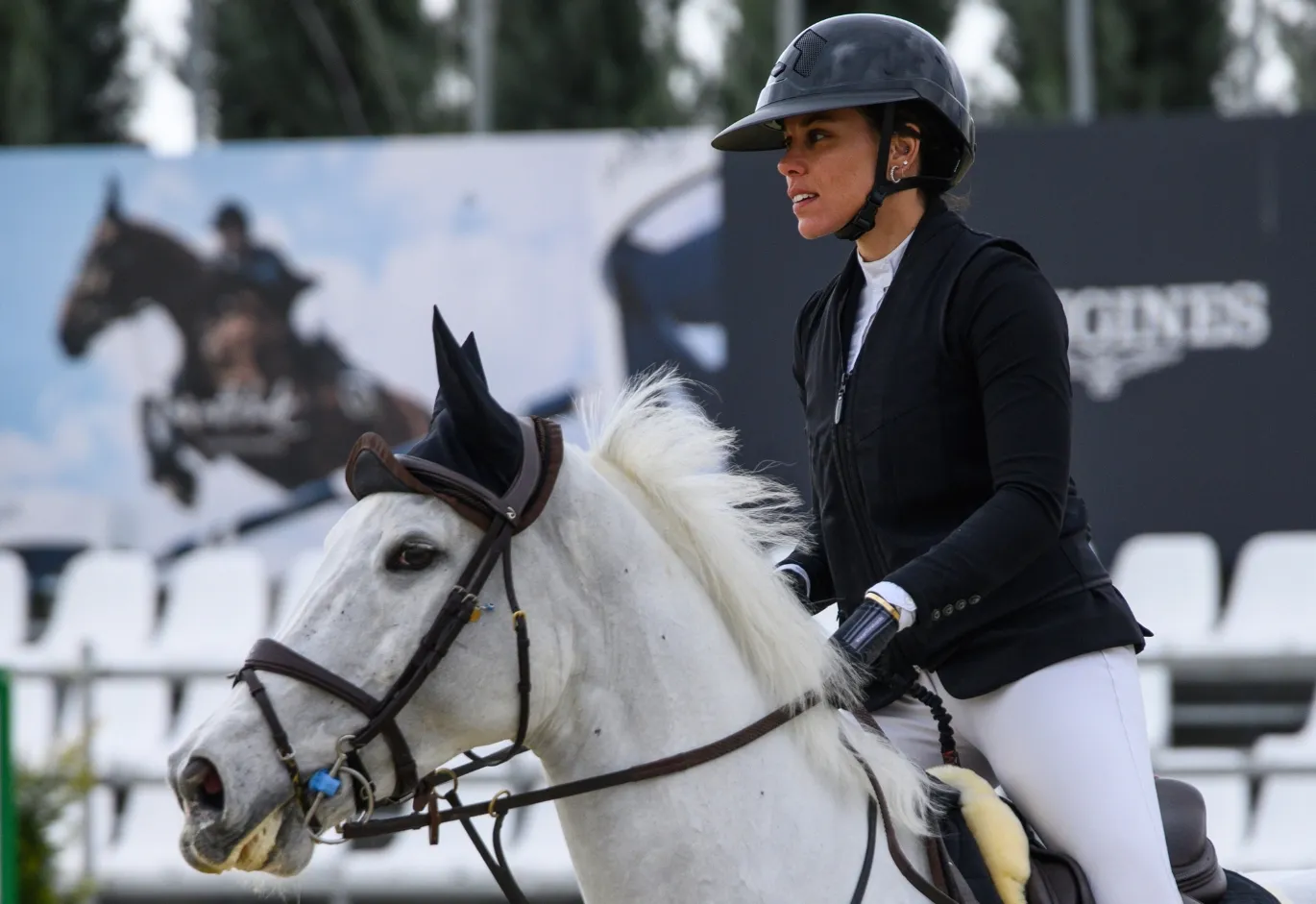 Female equestrian in full riding attire mounted on a white horse during an event.
