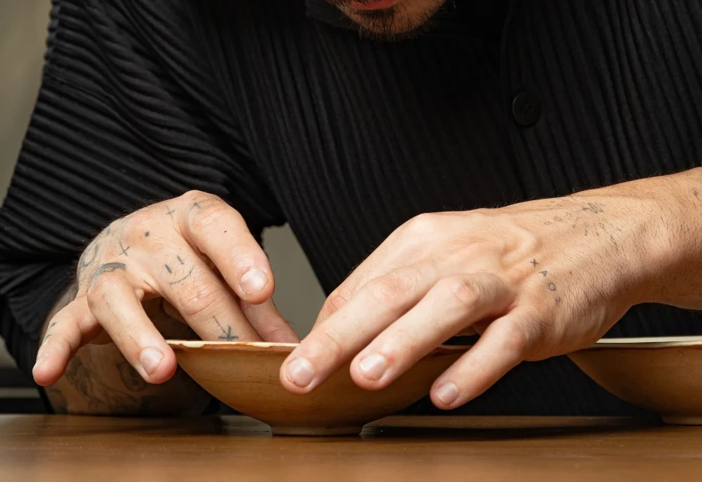 Close-up of a chef’s tattooed hands carefully plating a dish in shallow ceramic bowls