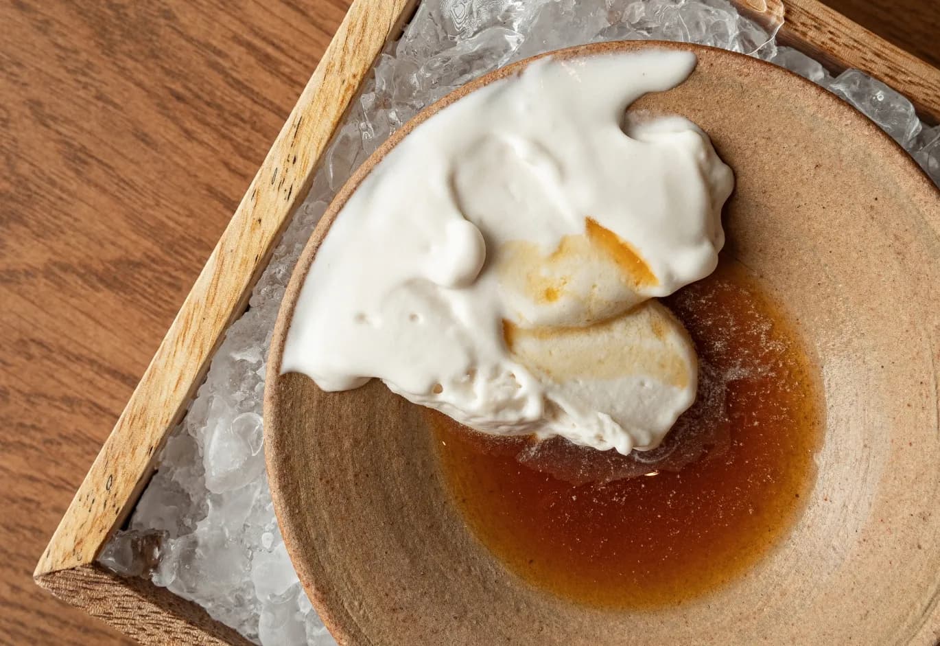 Gourmet dessert with white cream foam and rich syrup served in a ceramic bowl over crushed ice