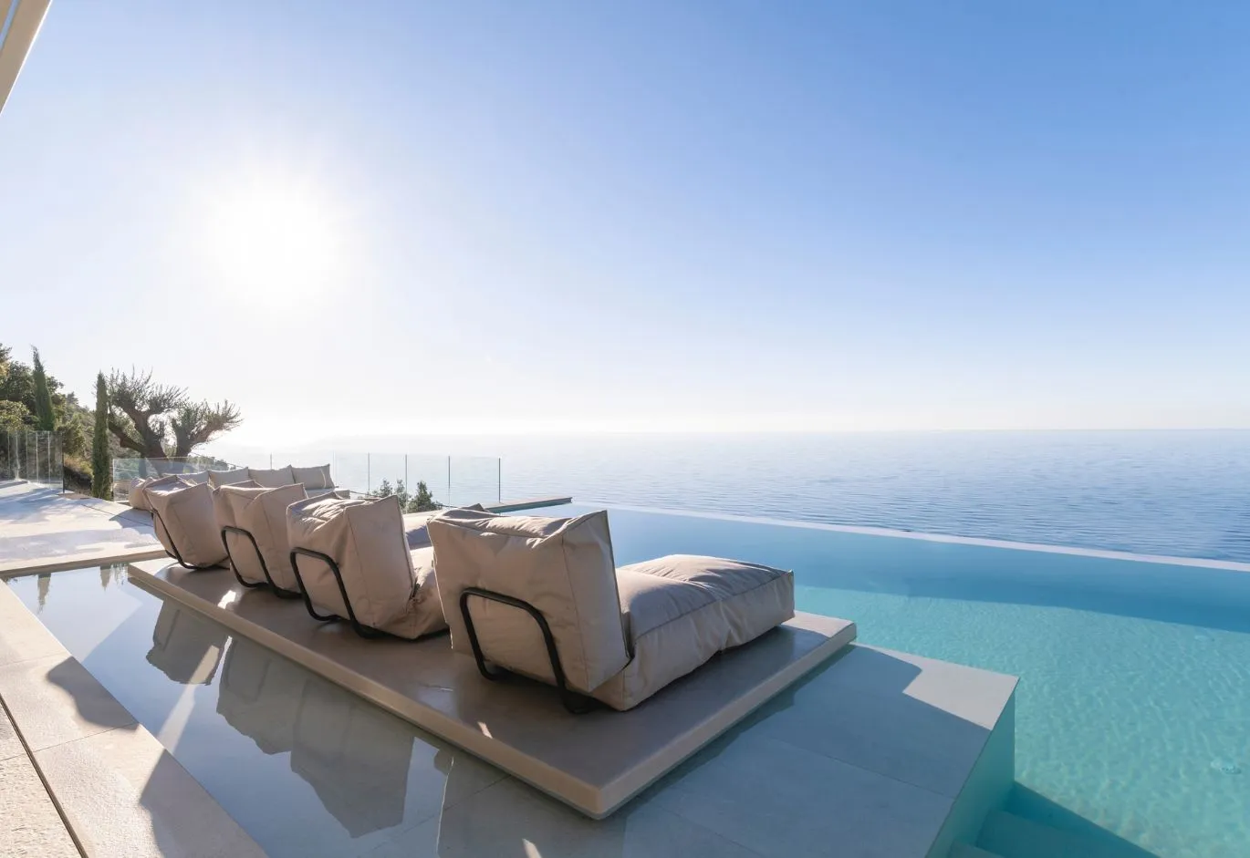 Luxury infinity pool with sunbeds integrated into the water overlooking the open sea under bright sunlight