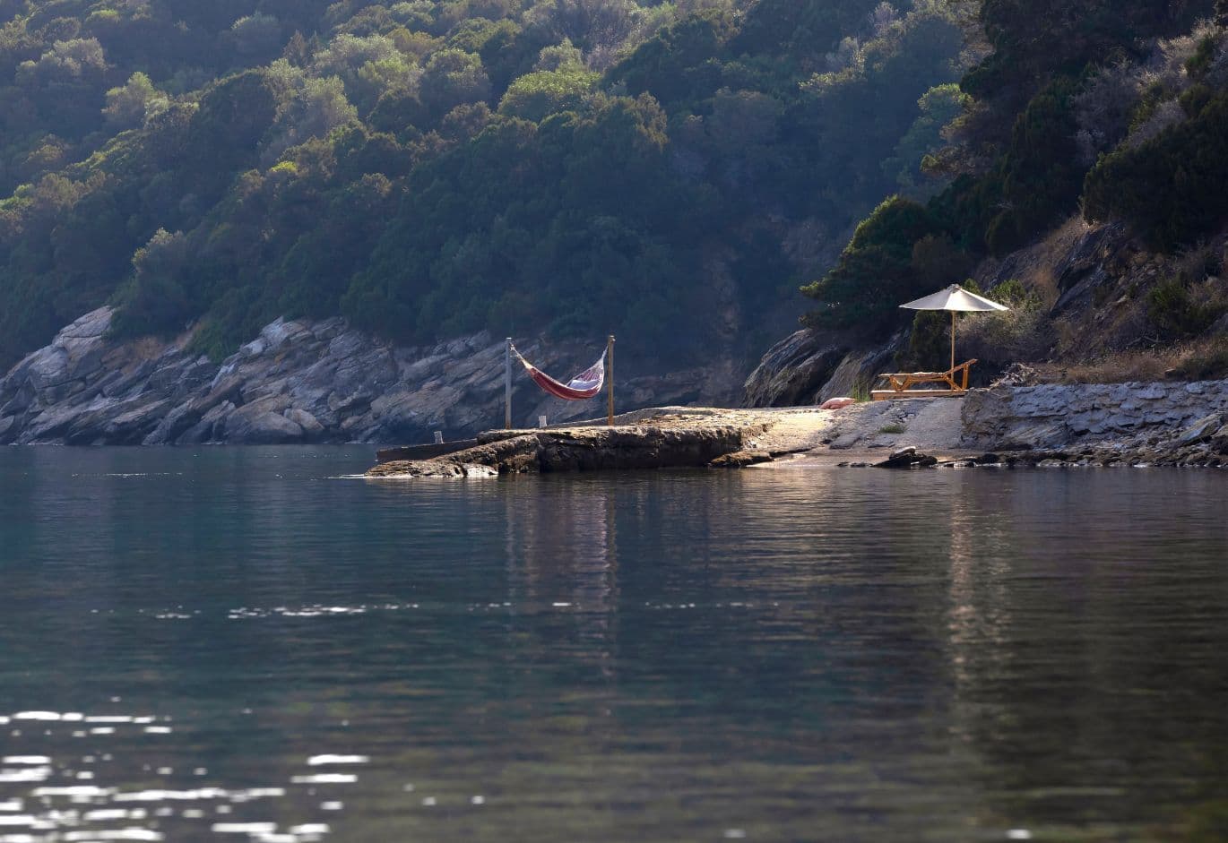Rocky coastal edge featuring a small stone pier equipped with a hammock and a sun lounger.