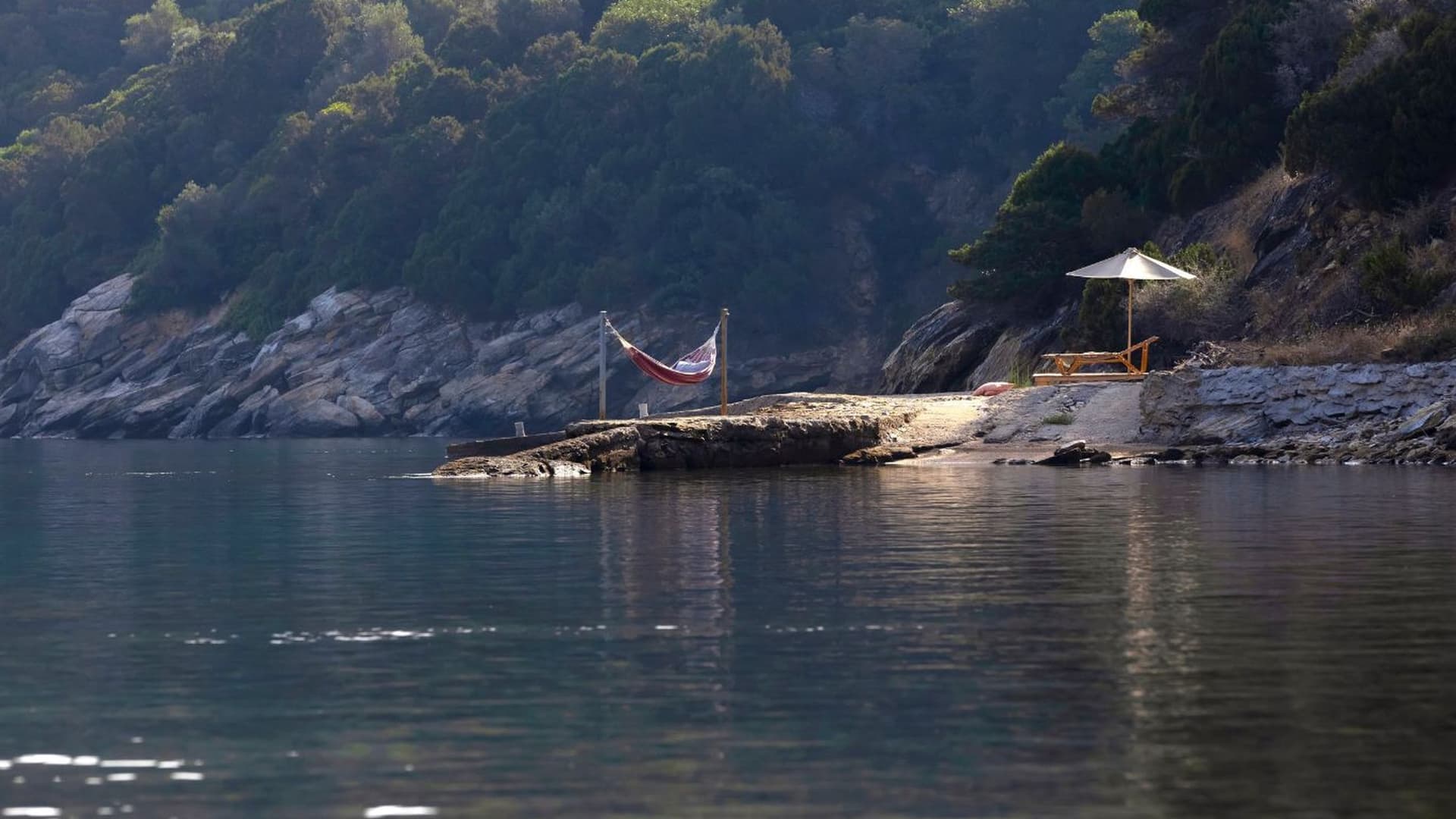 Rocky coastal edge featuring a small stone pier equipped with a hammock and a sun lounger.