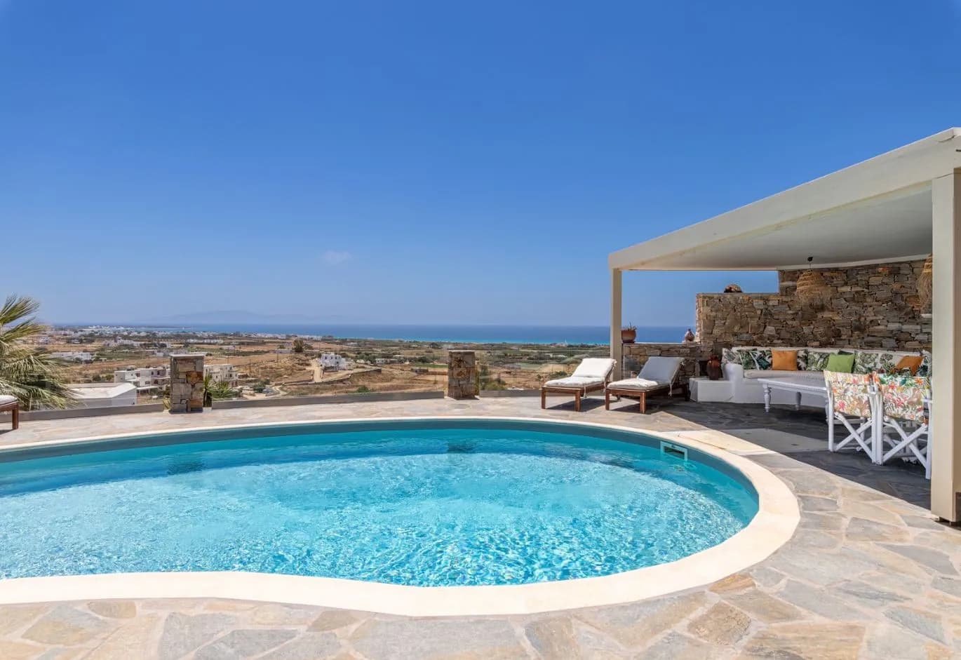Curved outdoor swimming pool and shaded lounge patio with a sweeping sea and landscape view