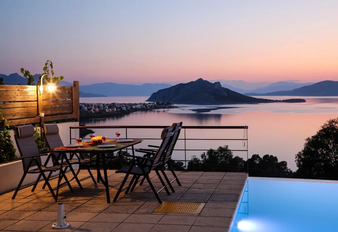 Sunset patio dining area next to an infinity pool with a panoramic view of the sea and mountains